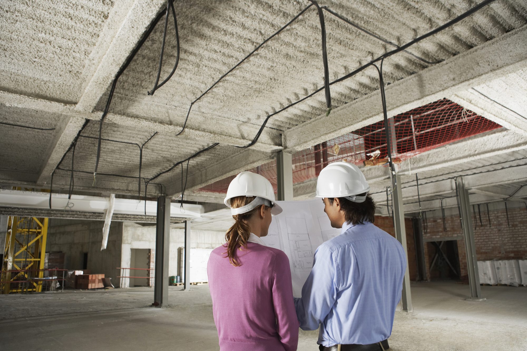 Rear view of architect and construction manager reading blueprint at site